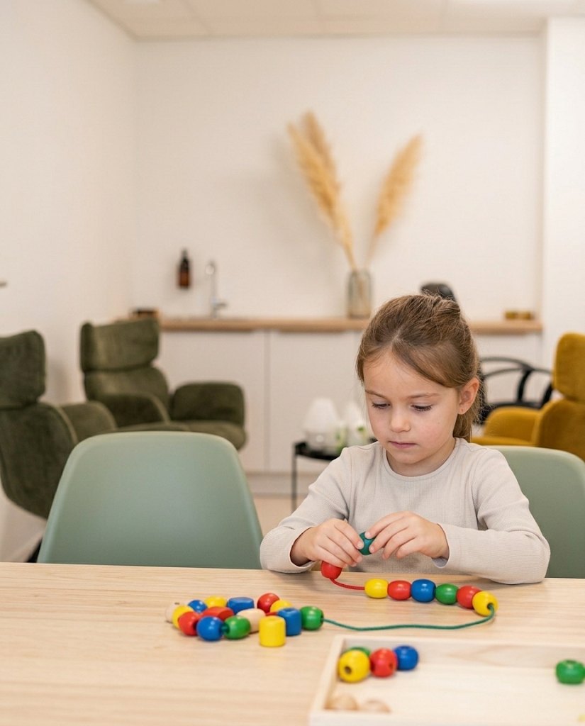 Une enfant enfile des perles en bois pendant une séance d'ergothérapie
